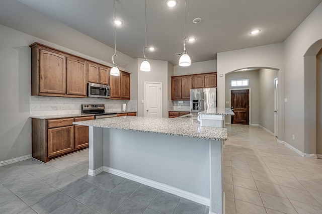 kitchen featuring decorative backsplash, stainless steel appliances, hanging light fixtures, and a center island with sink