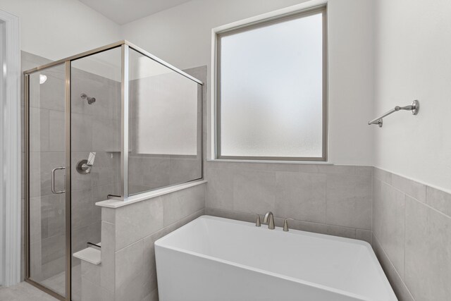 bathroom with a wealth of natural light, plus walk in shower, and tile walls