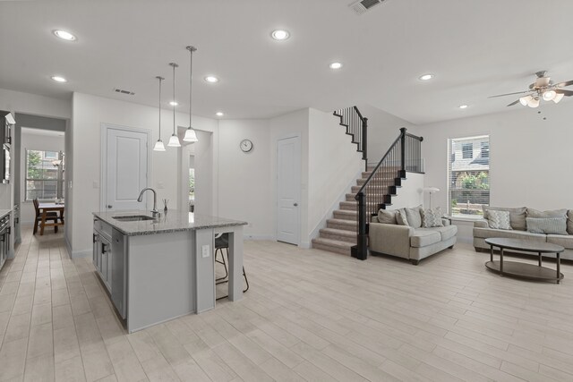 kitchen with a kitchen bar, sink, light stone counters, an island with sink, and ceiling fan