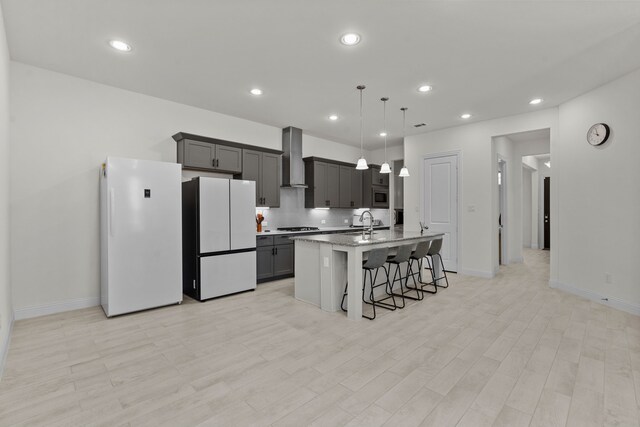 kitchen featuring wall chimney range hood, a kitchen bar, white refrigerator, and a kitchen island with sink