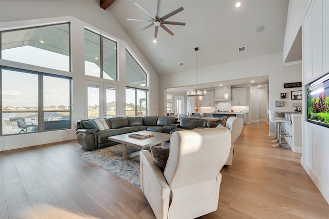 living room featuring high vaulted ceiling, beamed ceiling, light wood-type flooring, and ceiling fan with notable chandelier