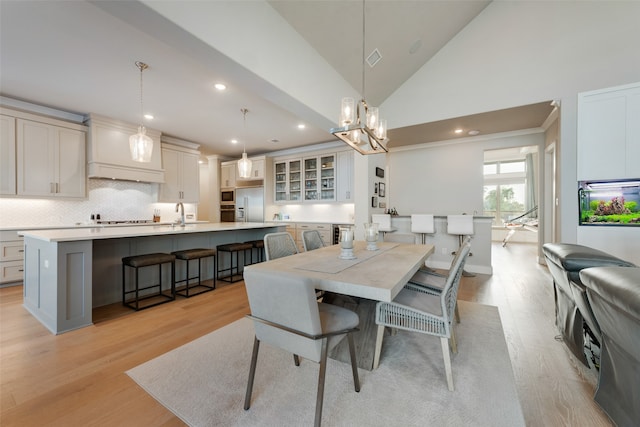 dining space with light hardwood / wood-style flooring, a chandelier, high vaulted ceiling, and sink