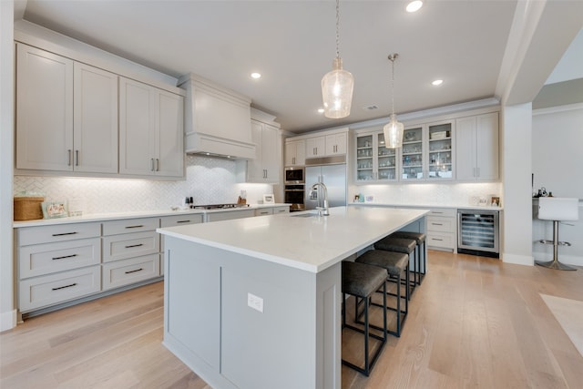 kitchen featuring a center island with sink, a kitchen bar, beverage cooler, custom exhaust hood, and light hardwood / wood-style floors