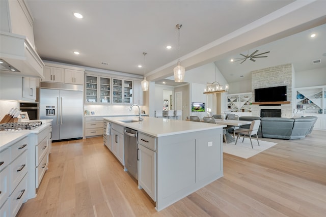 kitchen with appliances with stainless steel finishes, sink, a stone fireplace, white cabinets, and a kitchen island with sink