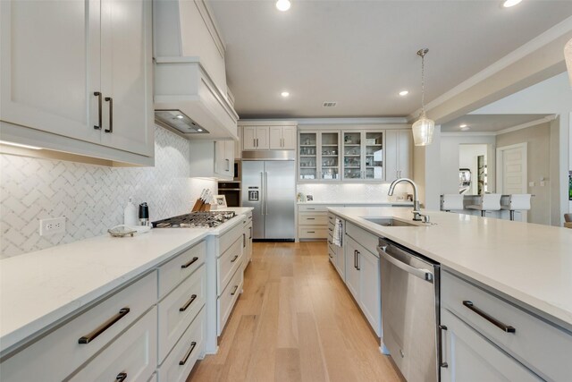 kitchen with white cabinets, appliances with stainless steel finishes, sink, light hardwood / wood-style floors, and decorative light fixtures