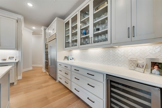 kitchen featuring tasteful backsplash, beverage cooler, white cabinetry, light wood-type flooring, and crown molding