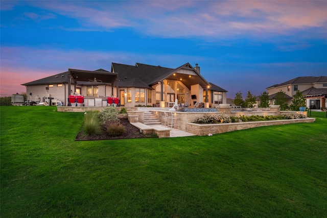 back house at dusk featuring a patio area and a lawn