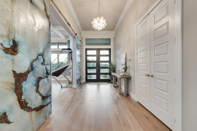 foyer with french doors, crown molding, a barn door, light wood-type flooring, and a chandelier