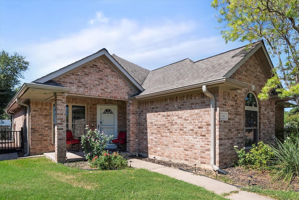 view of front of home with covered porch, brick siding, a front yard, and a shingled roof