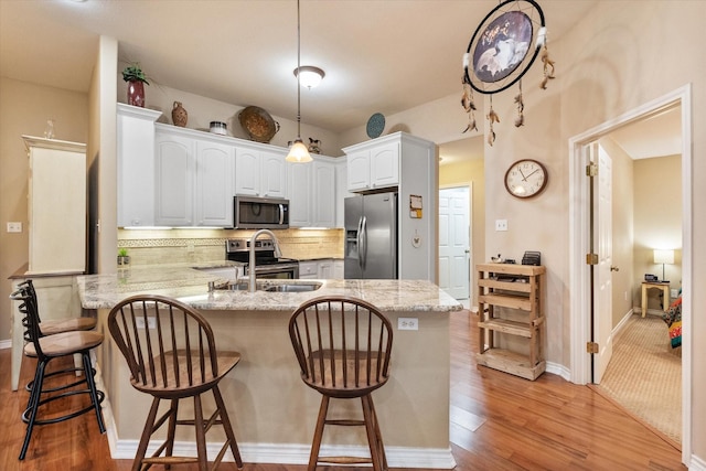 kitchen with white cabinets, appliances with stainless steel finishes, a peninsula, light stone countertops, and a sink