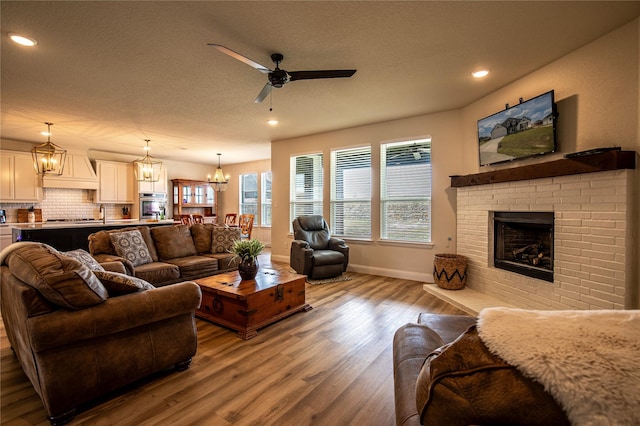 living room with hardwood / wood-style floors, ceiling fan with notable chandelier, and a brick fireplace