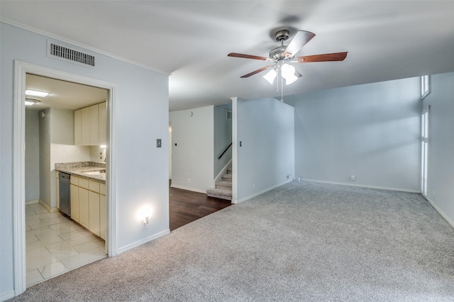 empty room with light colored carpet, a ceiling fan, baseboards, visible vents, and stairway