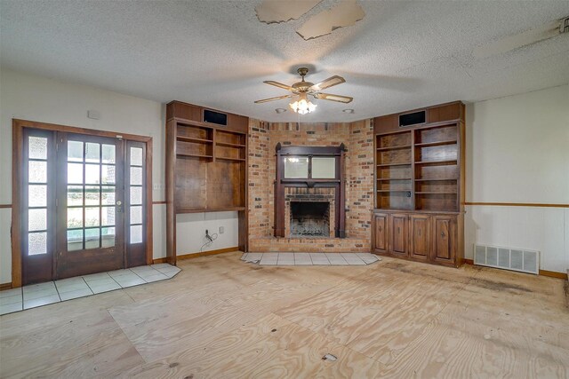 unfurnished living room with a fireplace, built in features, a textured ceiling, ceiling fan, and brick wall