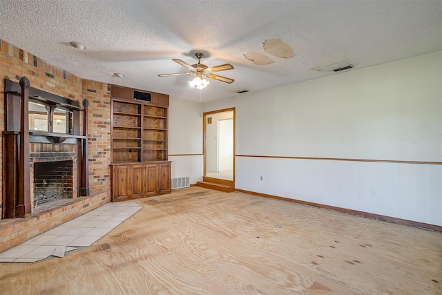 unfurnished living room featuring brick wall, built in features, a textured ceiling, ceiling fan, and a brick fireplace