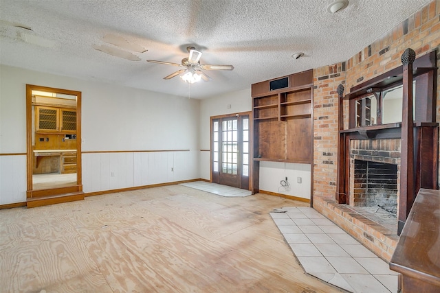 unfurnished living room featuring ceiling fan, brick wall, a textured ceiling, and a brick fireplace