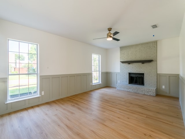 unfurnished living room with light wood-type flooring, brick wall, ceiling fan, and a brick fireplace