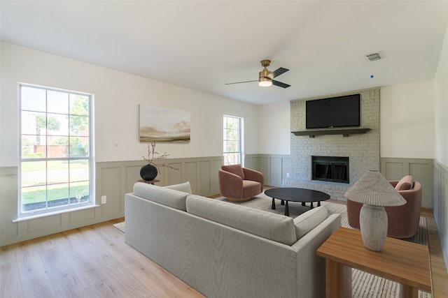 living room with a fireplace, brick wall, a wealth of natural light, and light hardwood / wood-style flooring