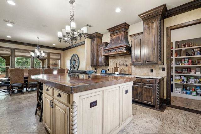 kitchen with custom range hood, a chandelier, ornamental molding, tasteful backsplash, and a kitchen island