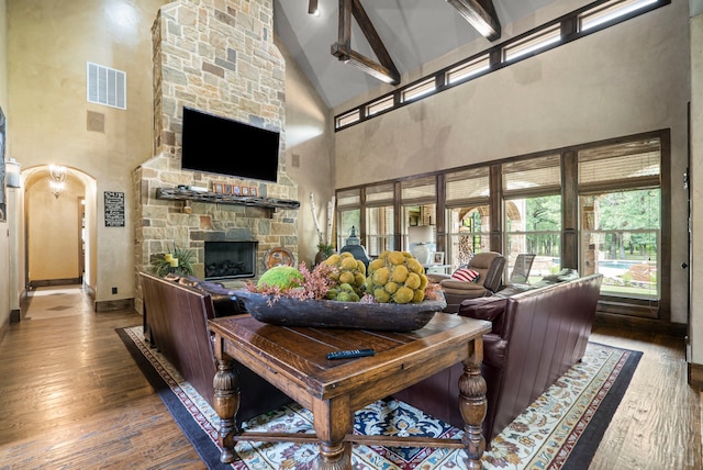 living room featuring beam ceiling, high vaulted ceiling, a stone fireplace, and hardwood / wood-style flooring