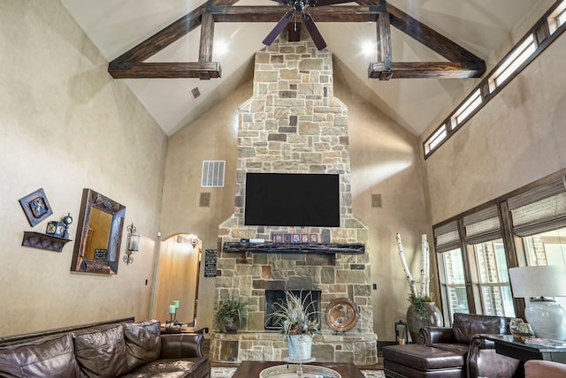 living room featuring ceiling fan, high vaulted ceiling, a stone fireplace, and beamed ceiling