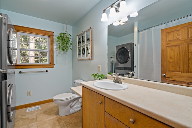 bathroom featuring tile patterned flooring, toilet, vanity, and stacked washer / dryer