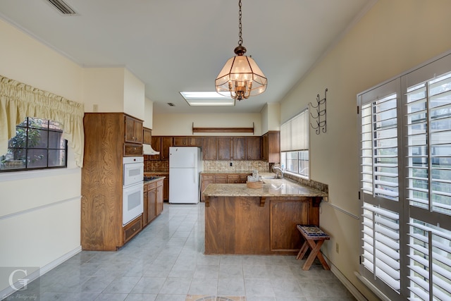 kitchen with tasteful backsplash, white appliances, kitchen peninsula, hanging light fixtures, and range hood