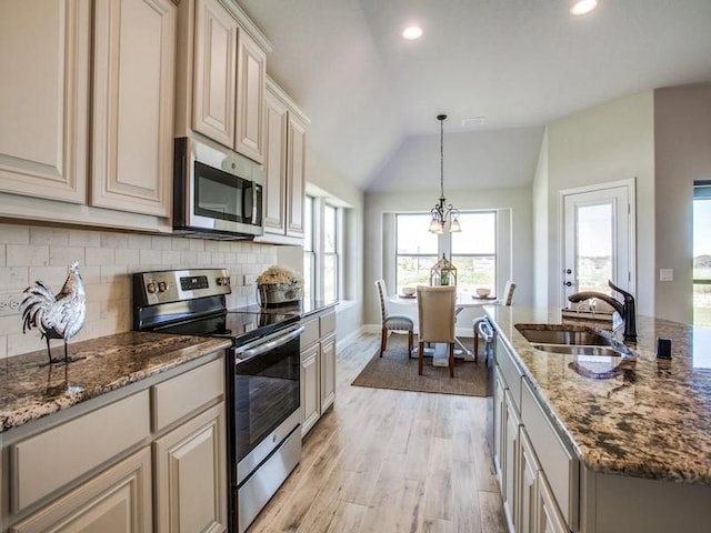 kitchen with appliances with stainless steel finishes, lofted ceiling, decorative light fixtures, sink, and cream cabinetry