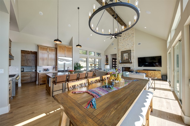 dining room with light hardwood / wood-style flooring, an inviting chandelier, brick wall, high vaulted ceiling, and a stone fireplace