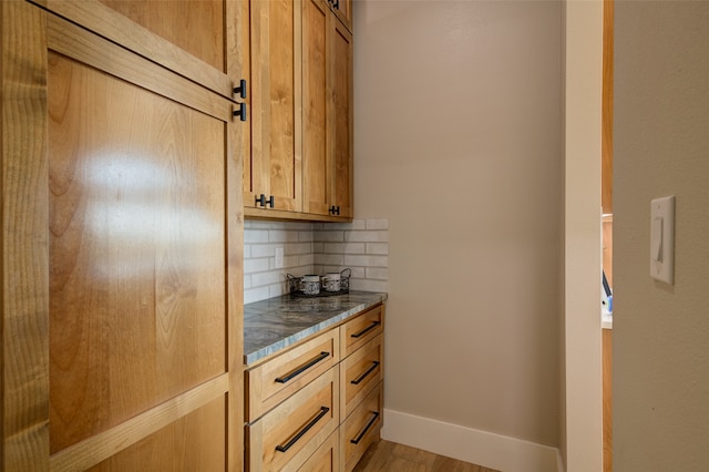 kitchen with light wood-type flooring, dark stone counters, and decorative backsplash