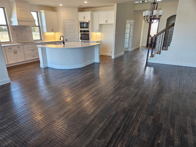 kitchen with premium range hood, white cabinetry, an island with sink, built in microwave, and oven