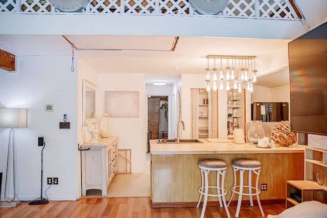 kitchen with sink, light hardwood / wood-style flooring, pendant lighting, and a kitchen bar