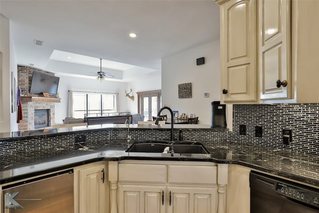 kitchen featuring black dishwasher, a stone fireplace, stainless steel dishwasher, a tray ceiling, and ceiling fan