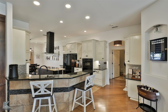 kitchen featuring a kitchen breakfast bar, decorative backsplash, light hardwood / wood-style floors, kitchen peninsula, and black appliances