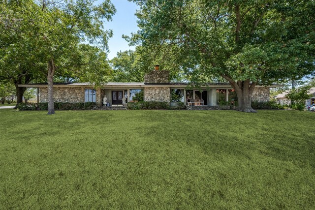 view of front of house with stone siding, a chimney, and a front lawn