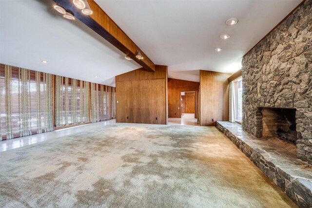 unfurnished living room with carpet, a fireplace, wood walls, and lofted ceiling with beams