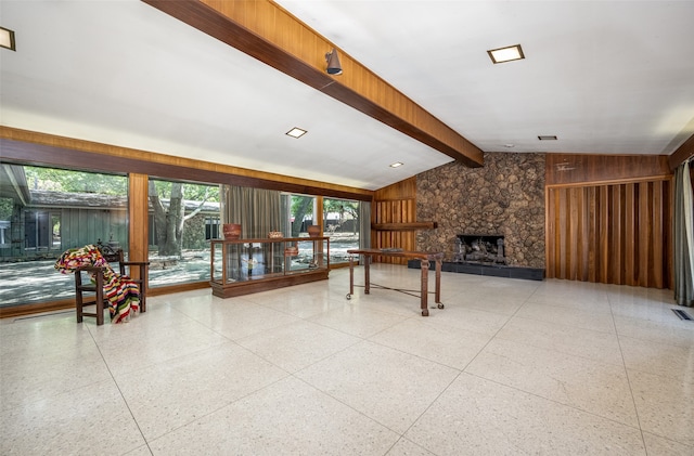 living room featuring wooden walls, a stone fireplace, and lofted ceiling with beams