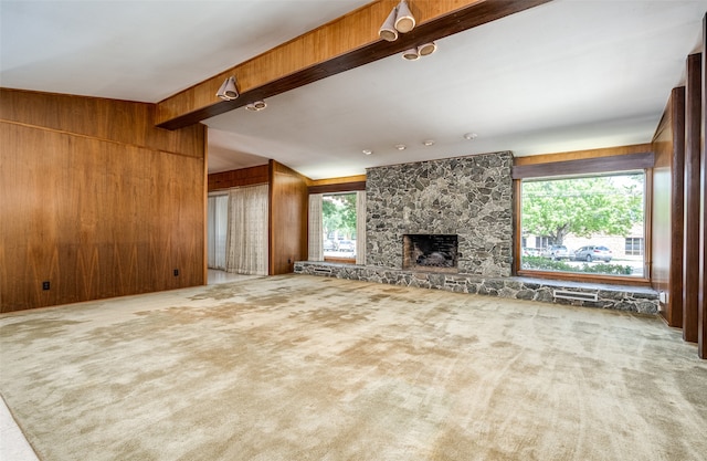 unfurnished living room featuring carpet floors, vaulted ceiling with beams, a stone fireplace, and wooden walls