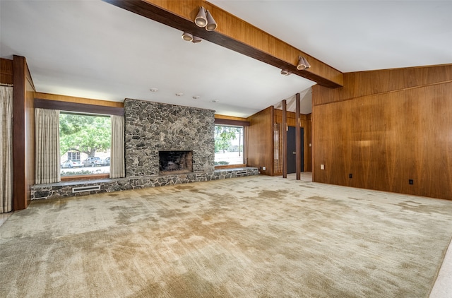 unfurnished living room featuring wooden walls, a stone fireplace, lofted ceiling with beams, and carpet