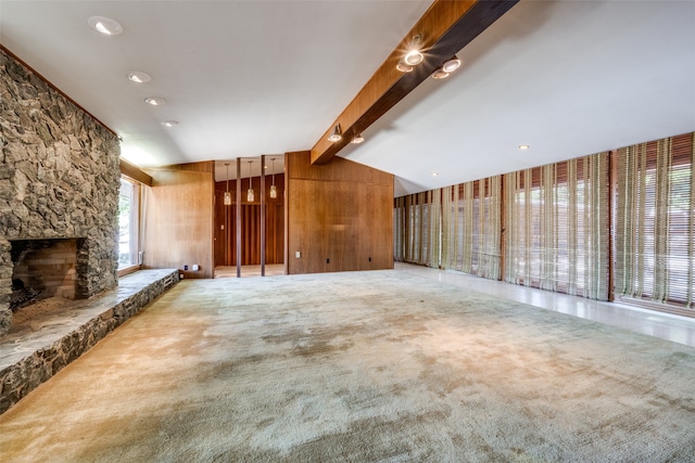 unfurnished living room featuring wooden walls, carpet floors, lofted ceiling with beams, and a stone fireplace