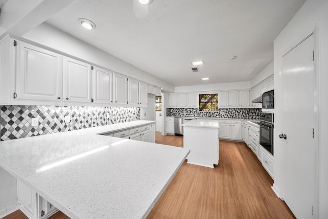 kitchen with white cabinetry, a center island, black appliances, and light wood-type flooring