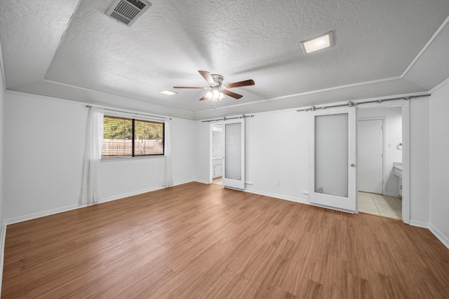 unfurnished bedroom featuring ensuite bath, ceiling fan, a barn door, light hardwood / wood-style floors, and vaulted ceiling