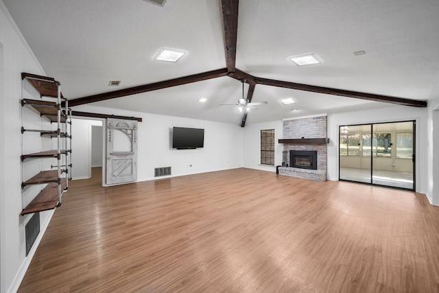 unfurnished living room featuring a textured ceiling, ceiling fan, light hardwood / wood-style flooring, a fireplace, and vaulted ceiling with beams