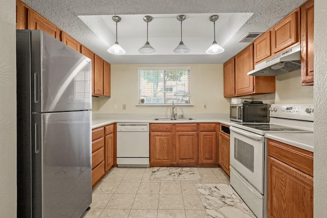 kitchen with decorative light fixtures, white appliances, sink, and a tray ceiling