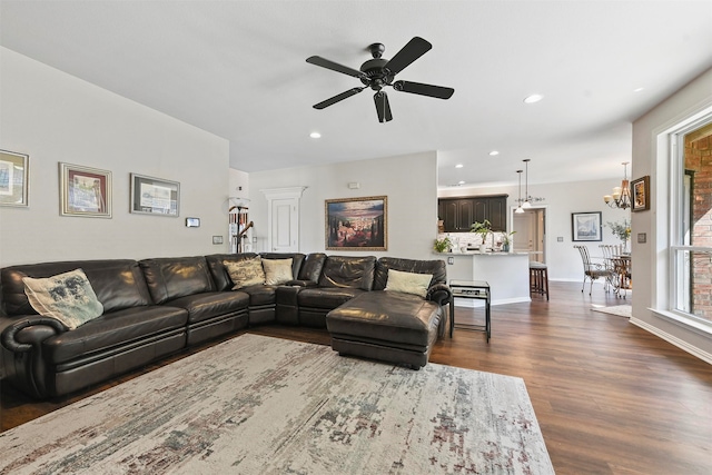 living room featuring ceiling fan with notable chandelier and dark wood-type flooring