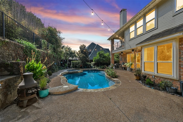 pool at dusk featuring a patio area and an in ground hot tub