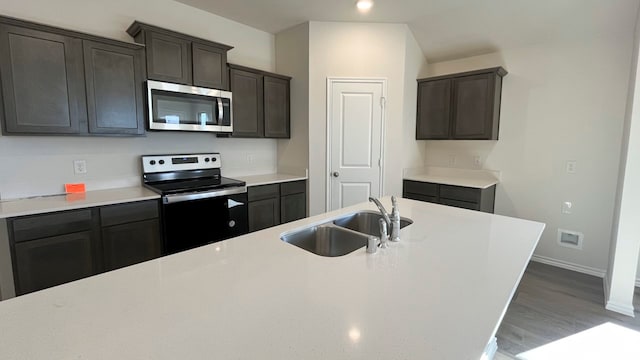 kitchen with dark brown cabinetry, sink, stainless steel appliances, and hardwood / wood-style flooring