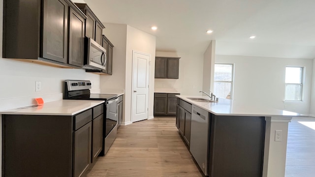 kitchen with sink, stainless steel appliances, an island with sink, light hardwood / wood-style floors, and dark brown cabinets