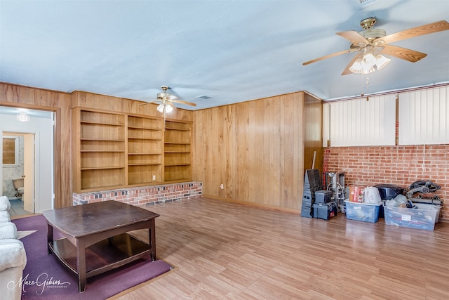 living room with ceiling fan, light wood-type flooring, wooden walls, and built in shelves