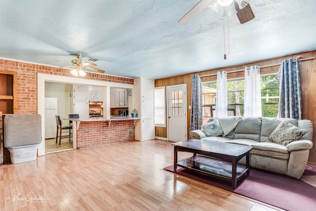 living room featuring ceiling fan, light hardwood / wood-style flooring, and wooden walls