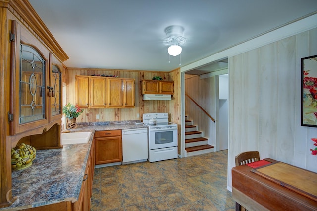 kitchen with white appliances, wooden walls, brown cabinets, under cabinet range hood, and a sink